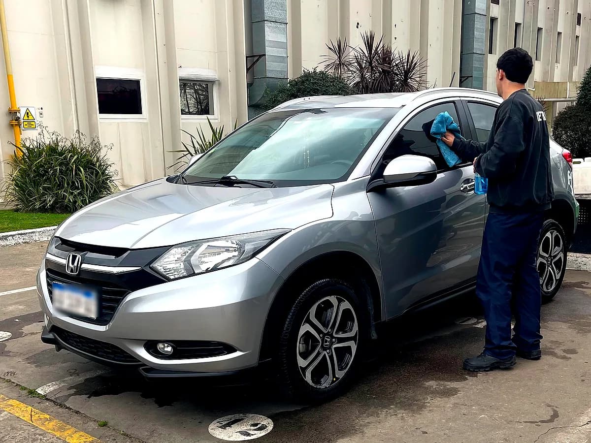 Un biowasher secando con un paño de microfibra una camioneta plateada en el estacionamiento de una planta industrial